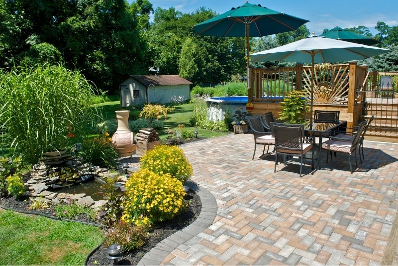Paved patio with outdoor dining setting, umbrellas and a garden pond